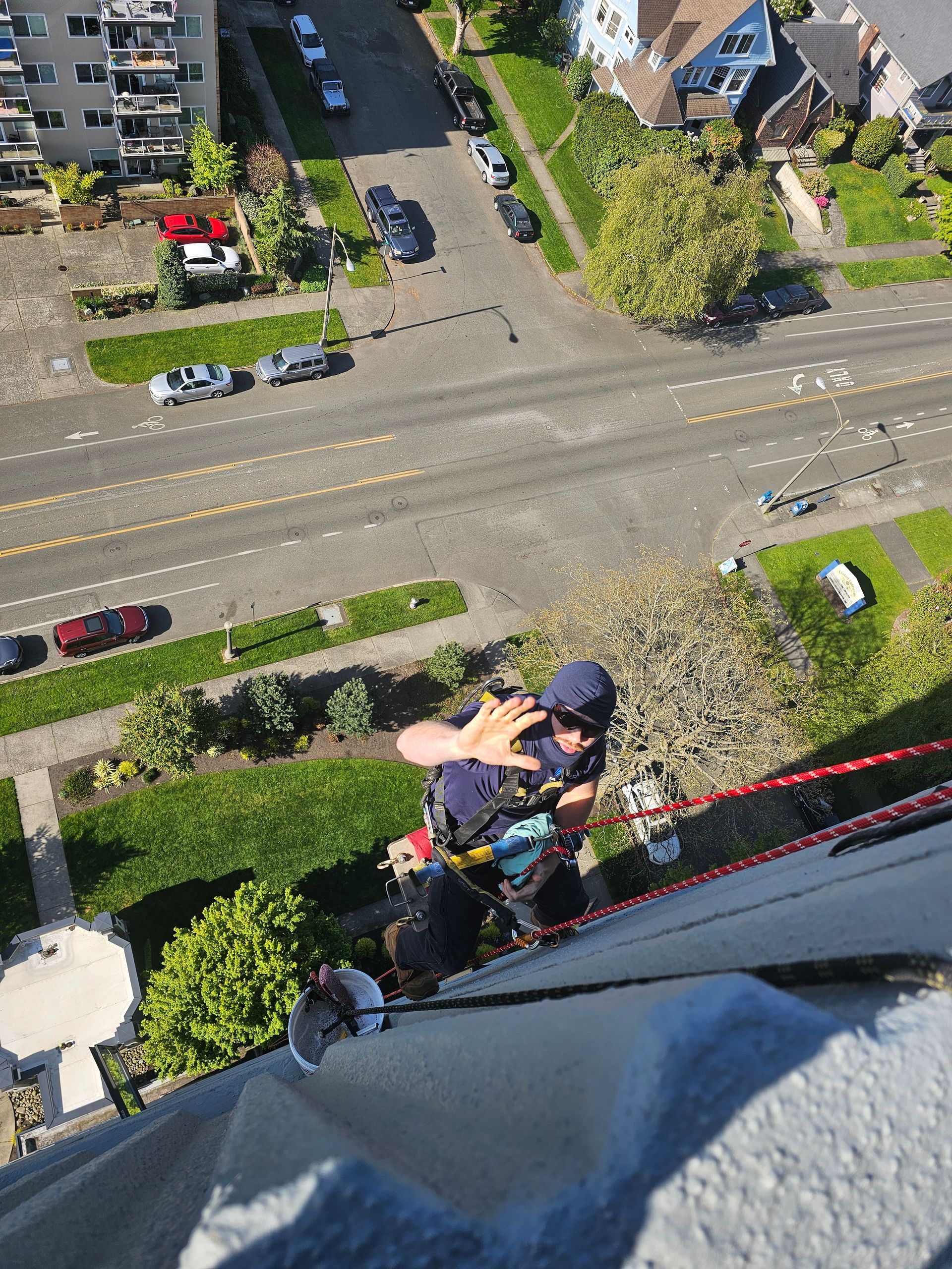 Two window washers on a building, one taking a selfie. City street view, sunny day.