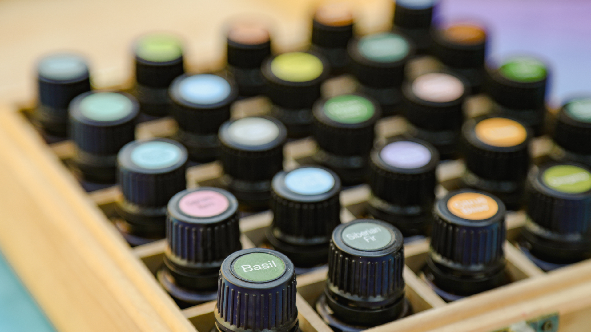Rows of colorful essential oil bottles in a wooden tray, viewed from above