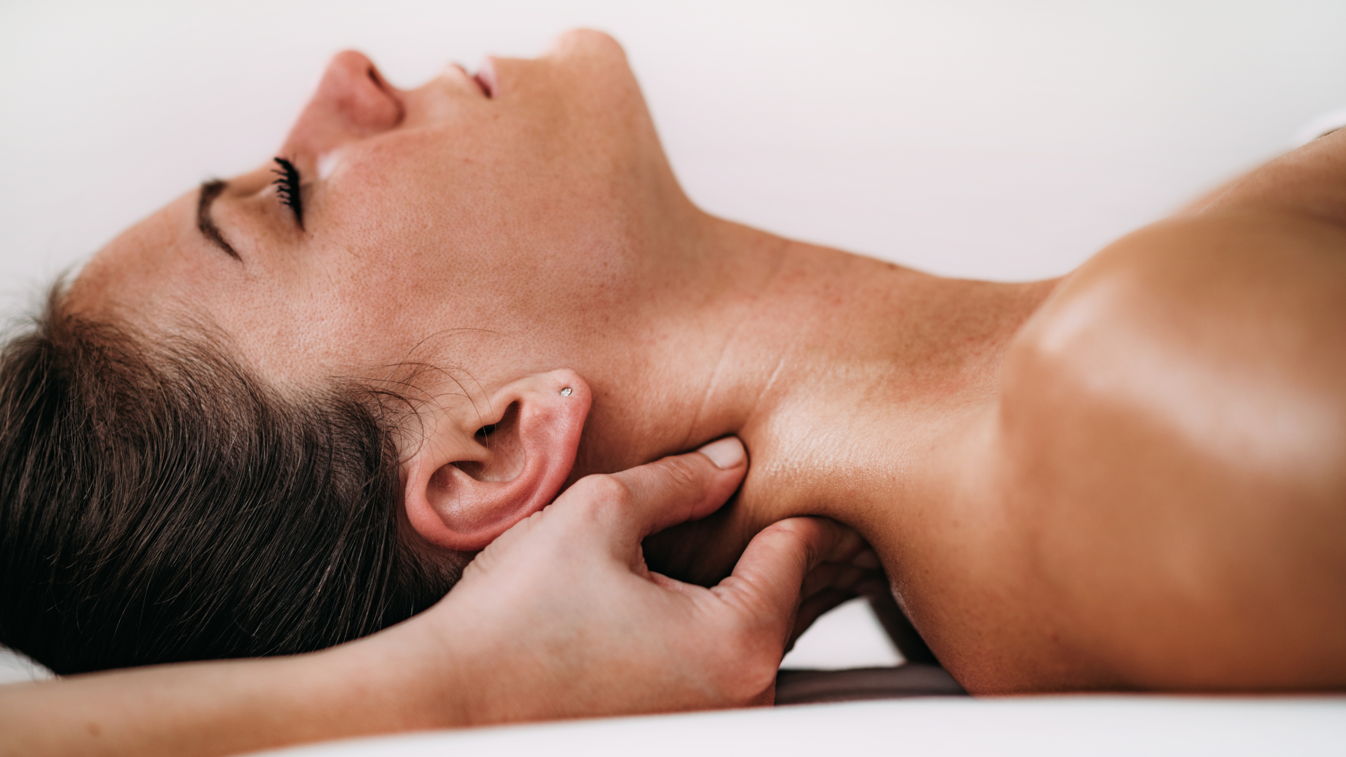 Person lying on a massage table while a hand massages the neck