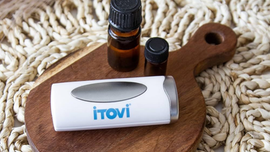 White iTovi device beside two small amber bottles on a wooden board