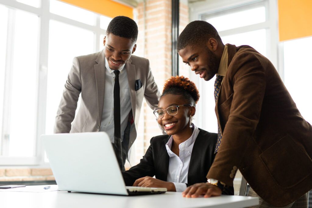 Three people looking at a laptop in an office. They are smiling.