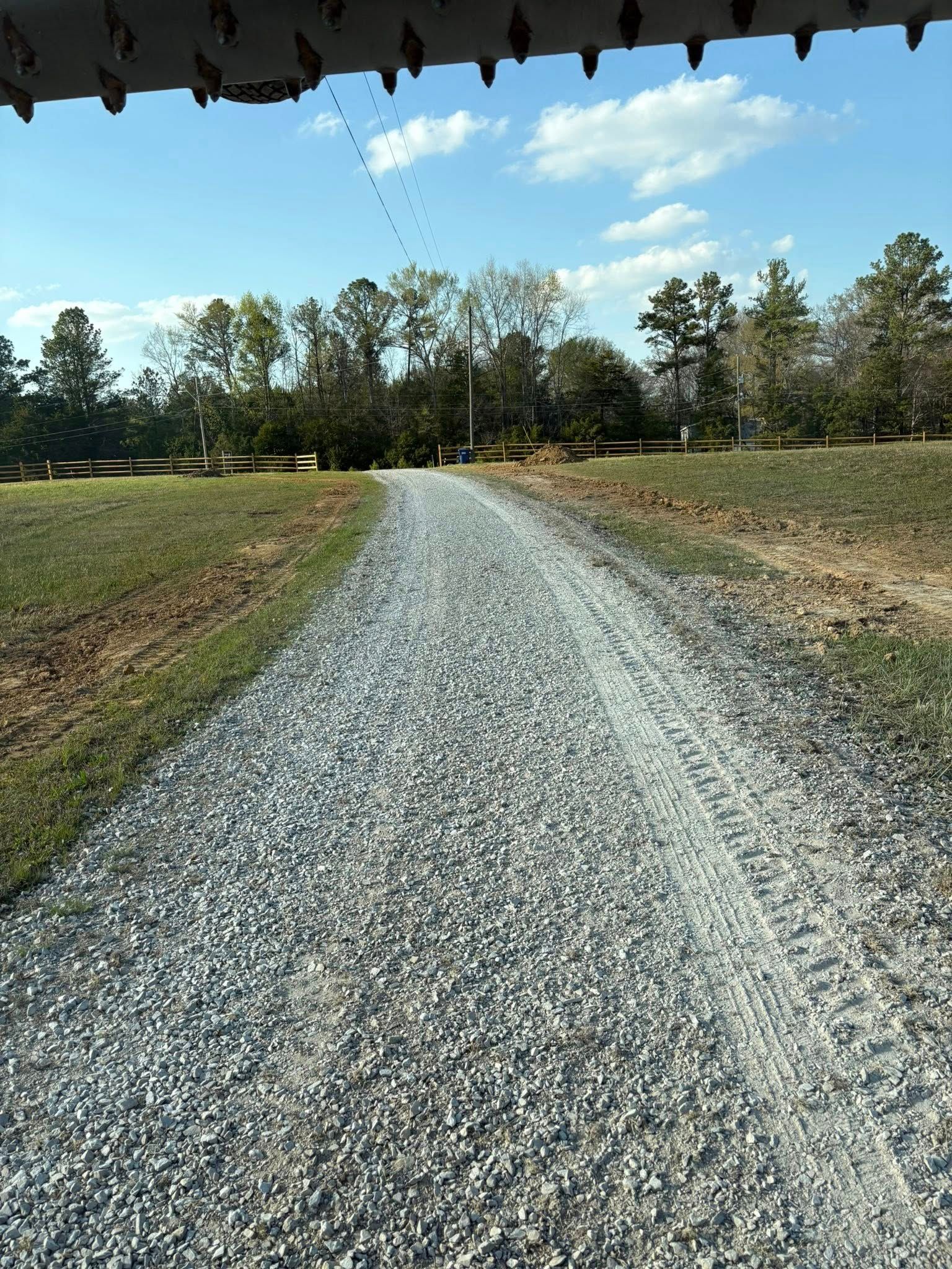 Gravel road curving through a wooded field under a blue sky with clouds.