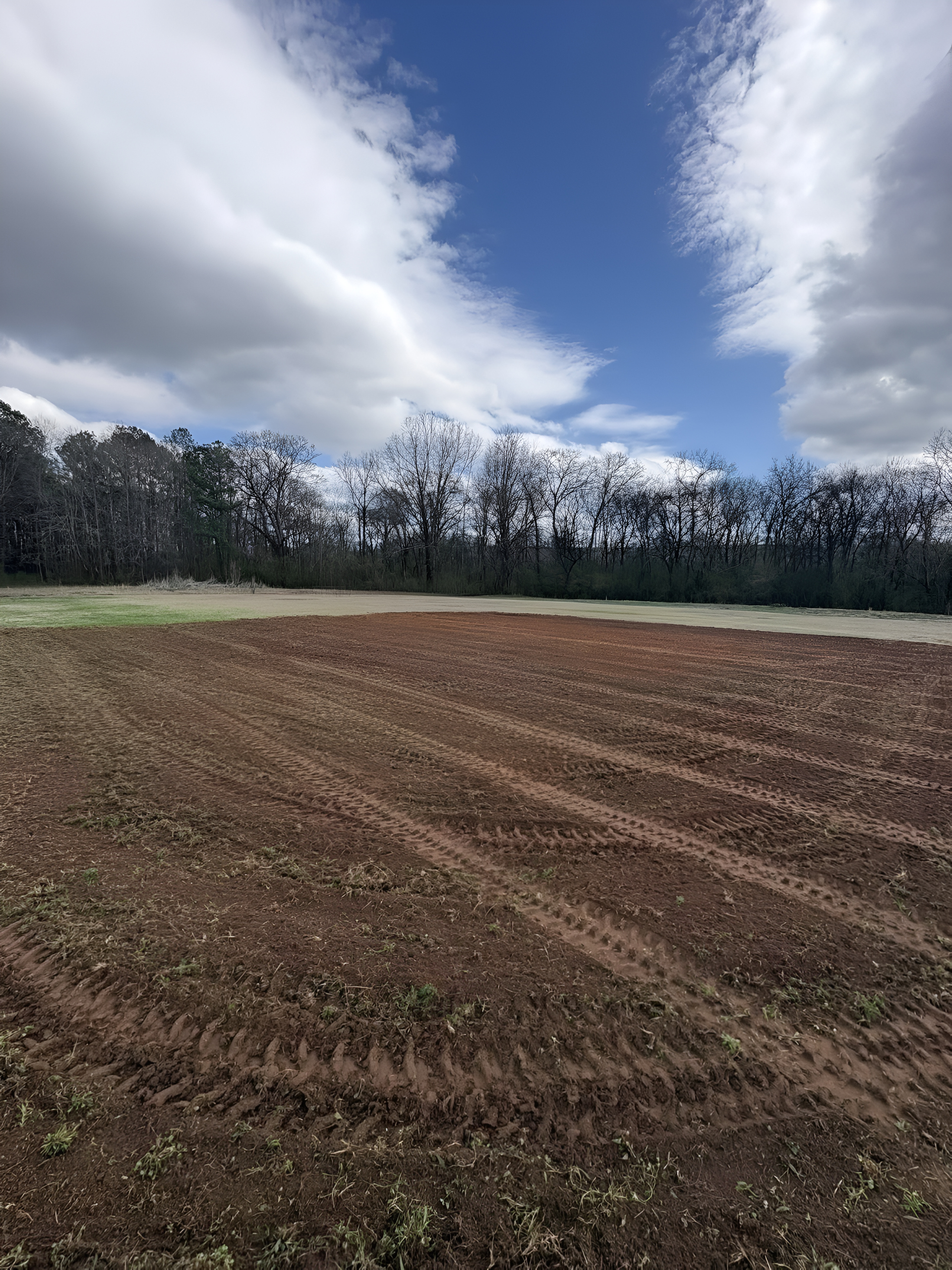 Plowed brown field beneath a cloudy blue sky with a line of trees in the distance
