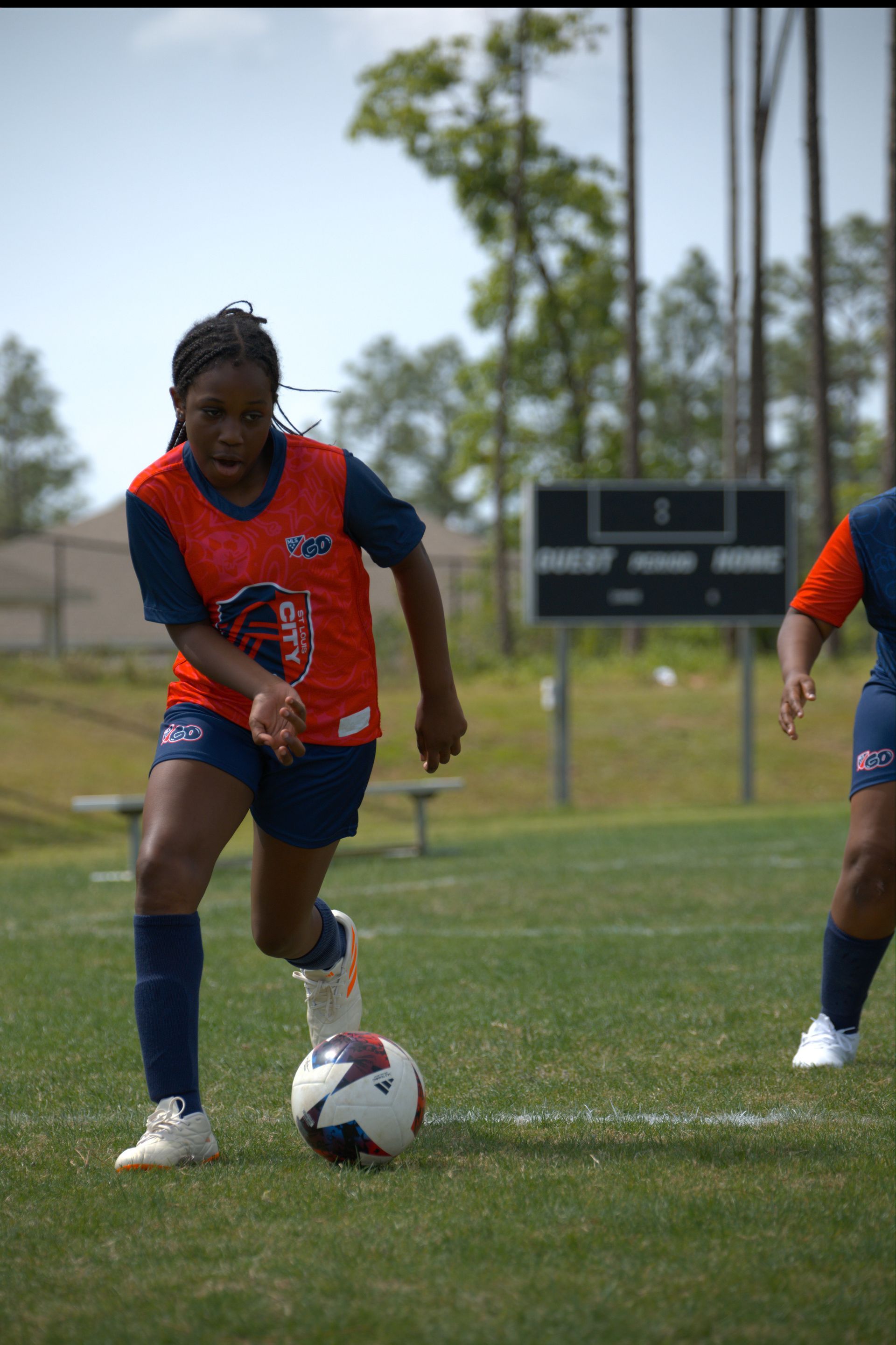 Soccer player in orange jersey dribbles ball on a grassy field.