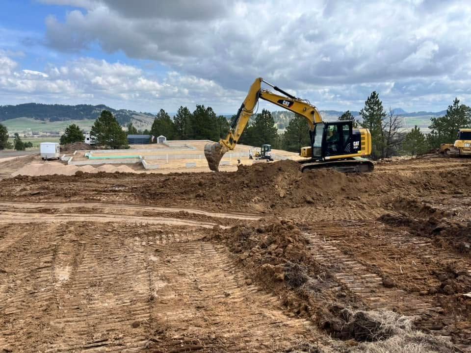 Yellow excavator clearing dirt on a muddy construction site under cloudy skies