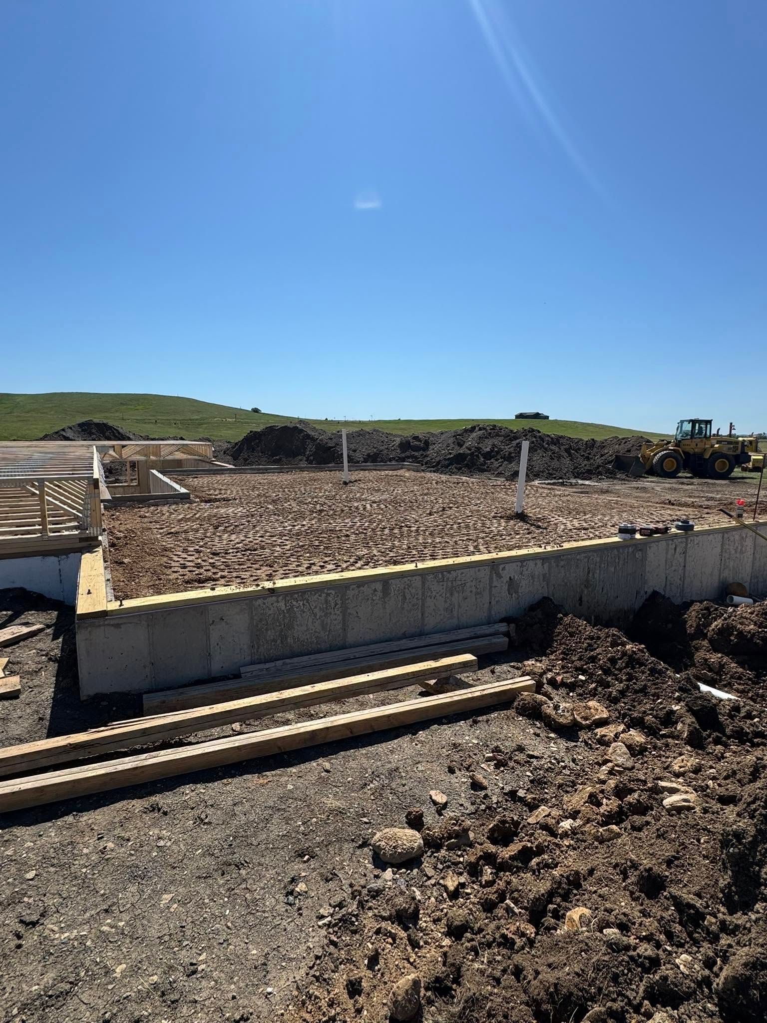 Construction site with concrete foundation walls, piles of gravel, and blue sky over a dirt foreground