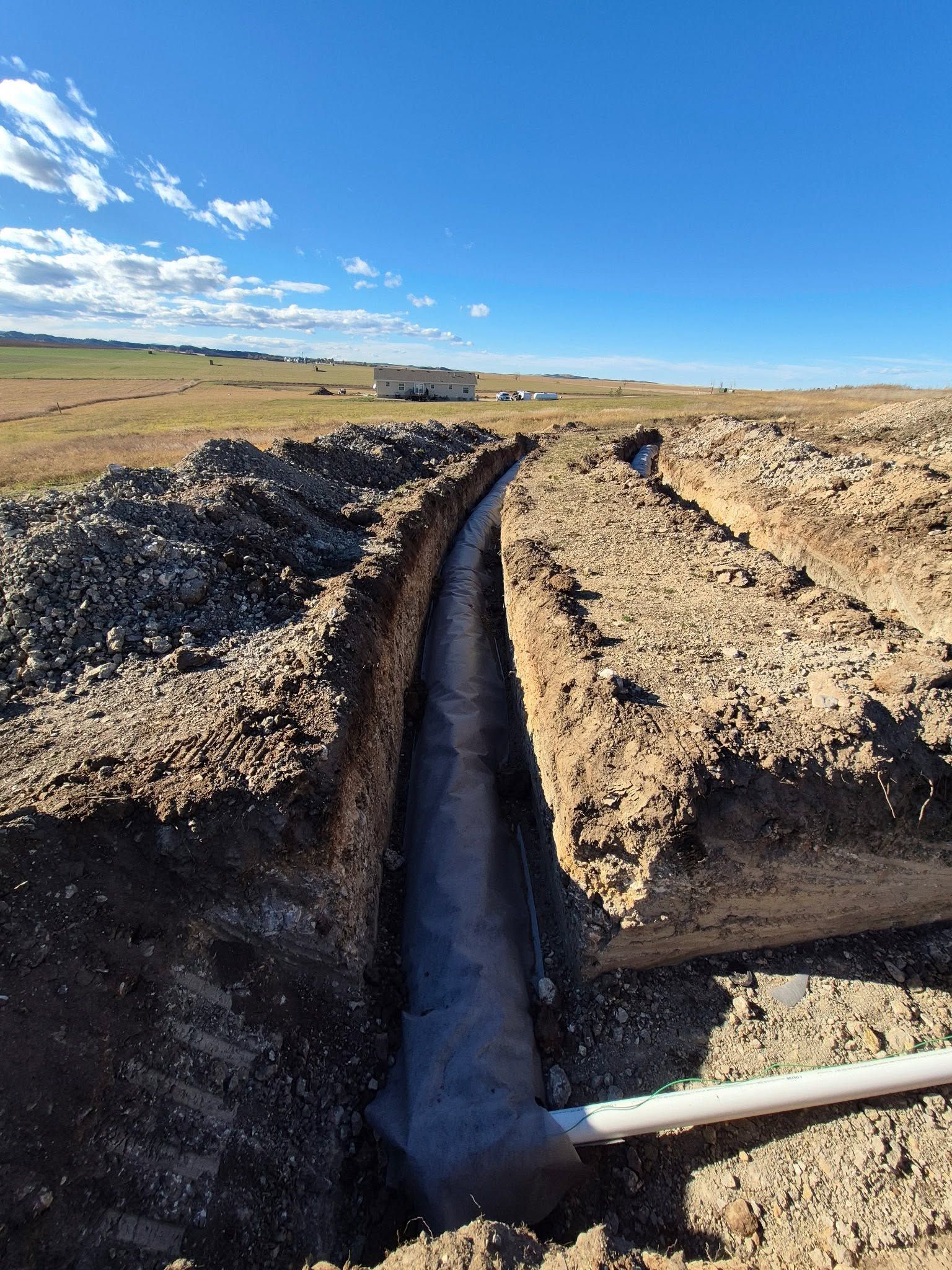 A narrow trench cut through a dry dirt field under a clear blue sky.