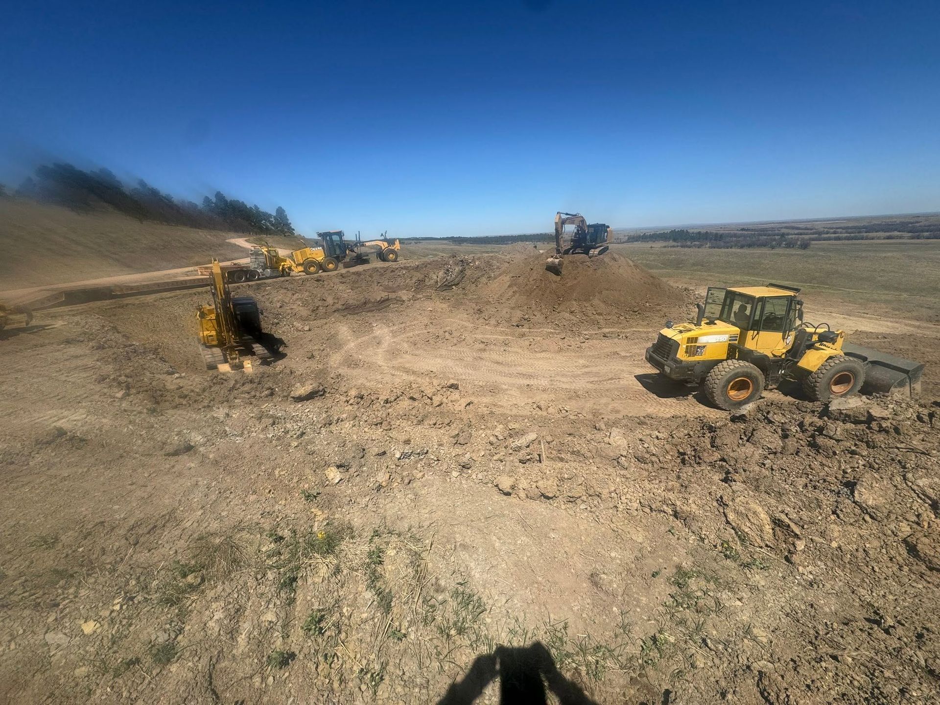 Construction site with yellow bulldozers grading a large dirt field under a clear blue sky