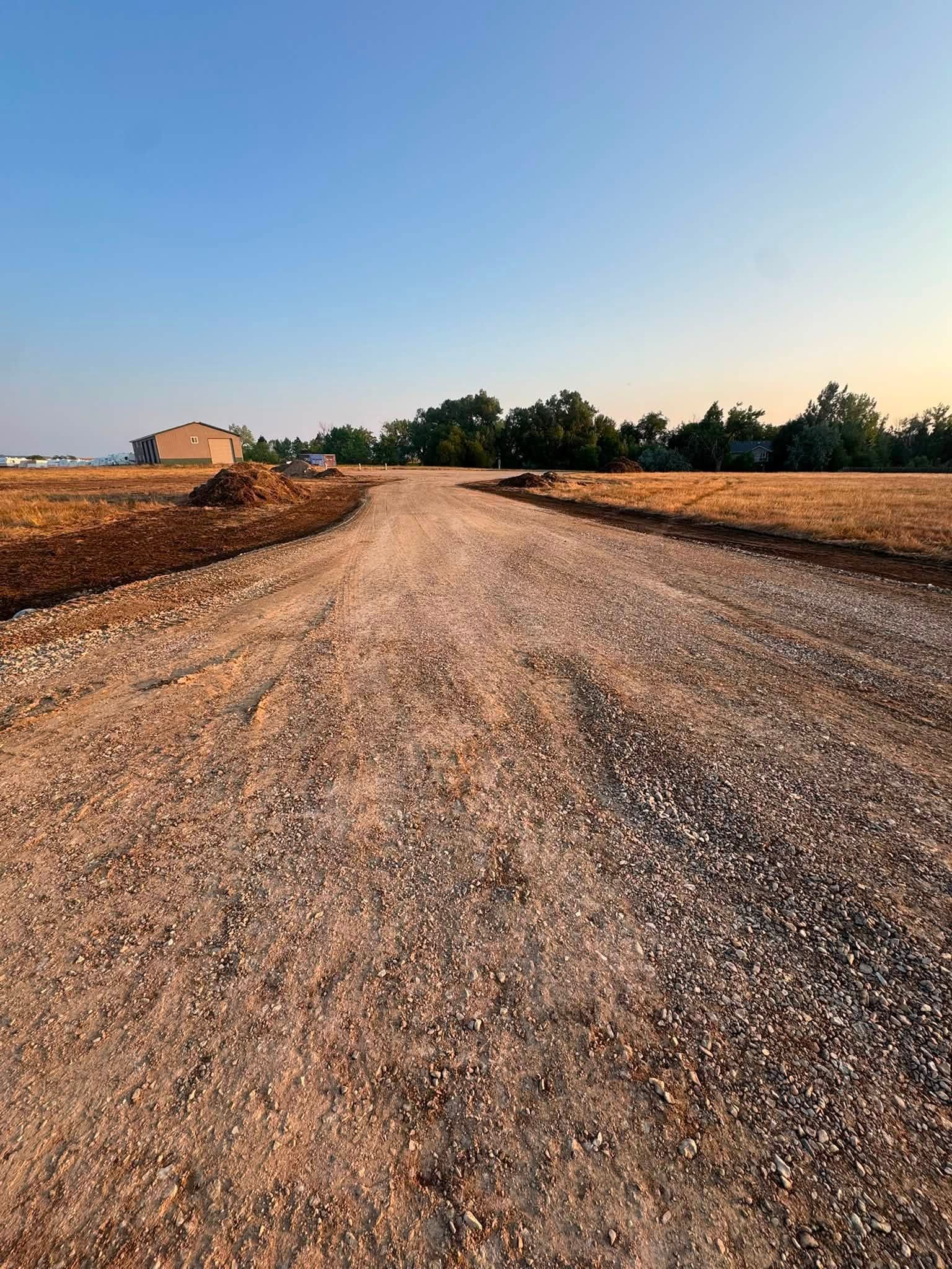 Gravel road curving through a dry rural field at sunset