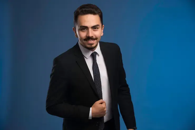 A man in a suit and tie is standing in front of a blue background.