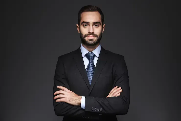 A man in a suit and tie is standing with his arms crossed.