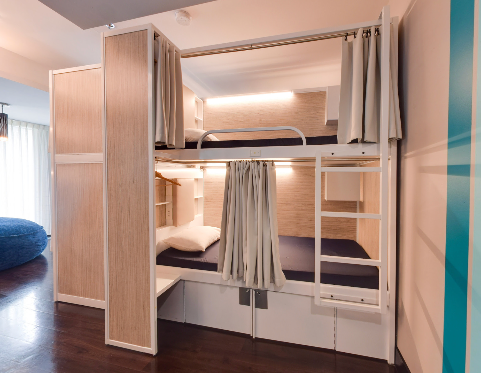 Lits superposés dans une chambre avec lambris clair, rideaux et rangements intégrés. Alèses bleues.