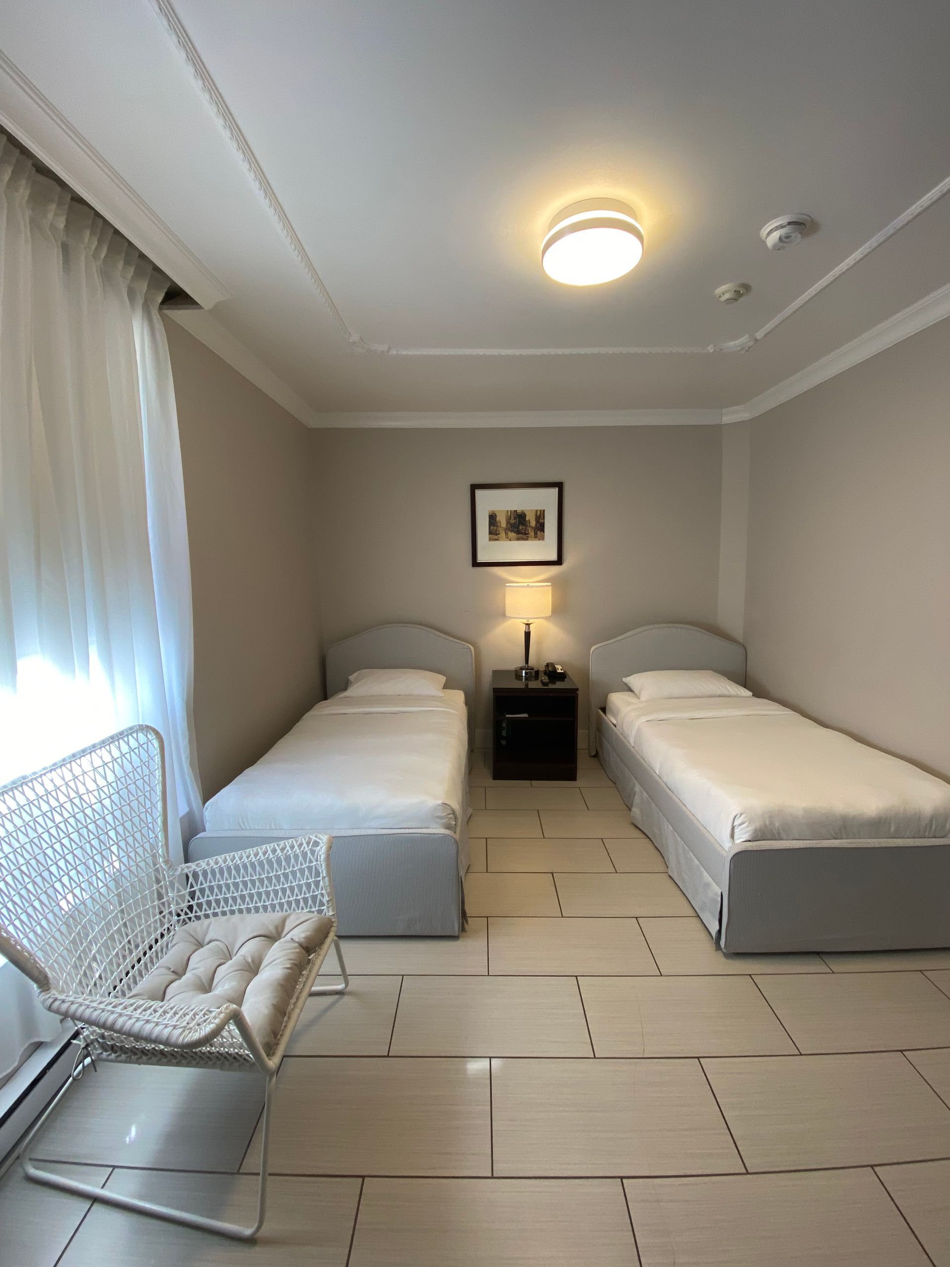 Deux lits jumeaux dans une chambre aux murs beiges avec des voilages blancs