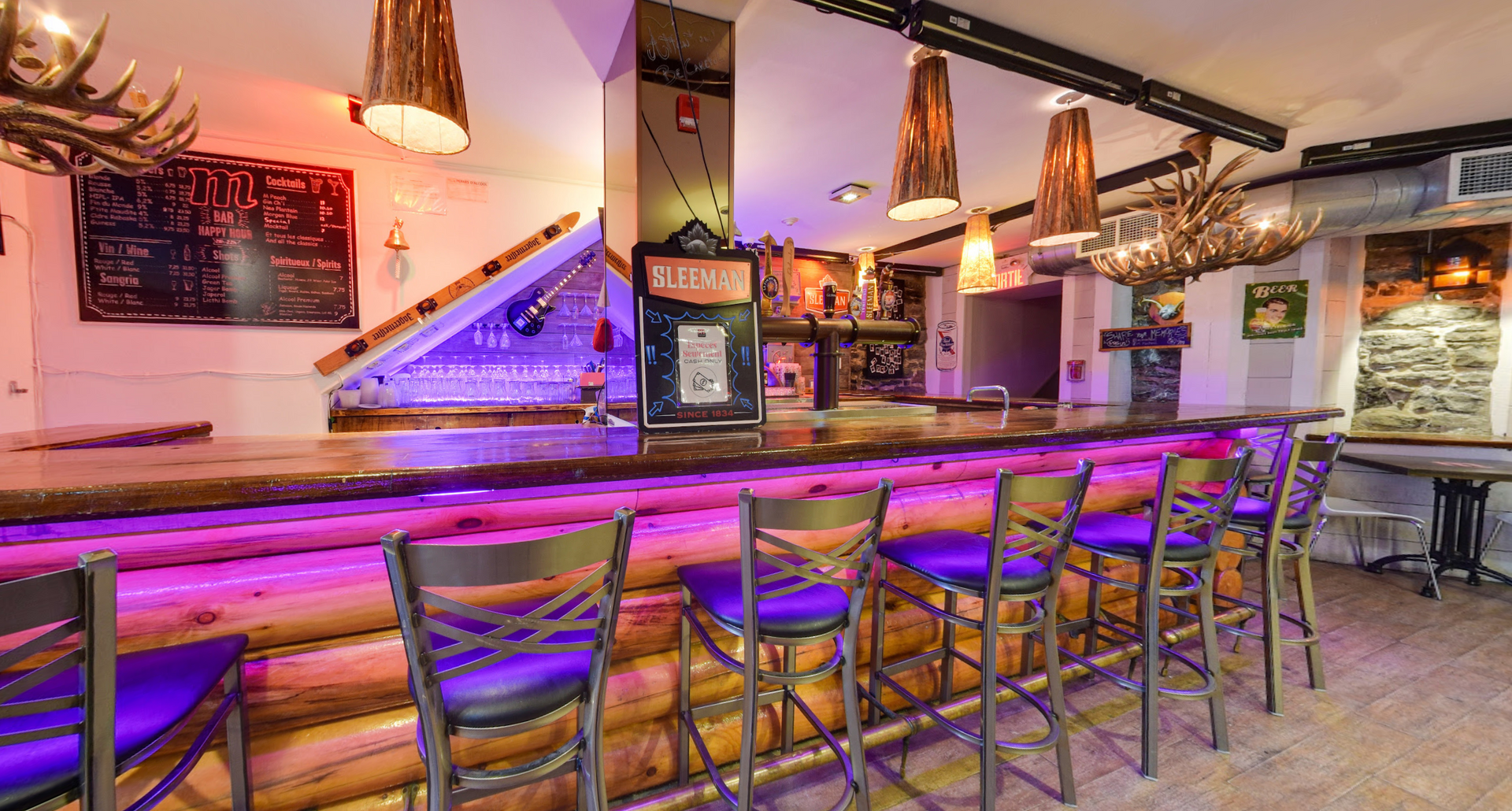 A long wooden bar with purple lights and purple chairs in a restaurant.