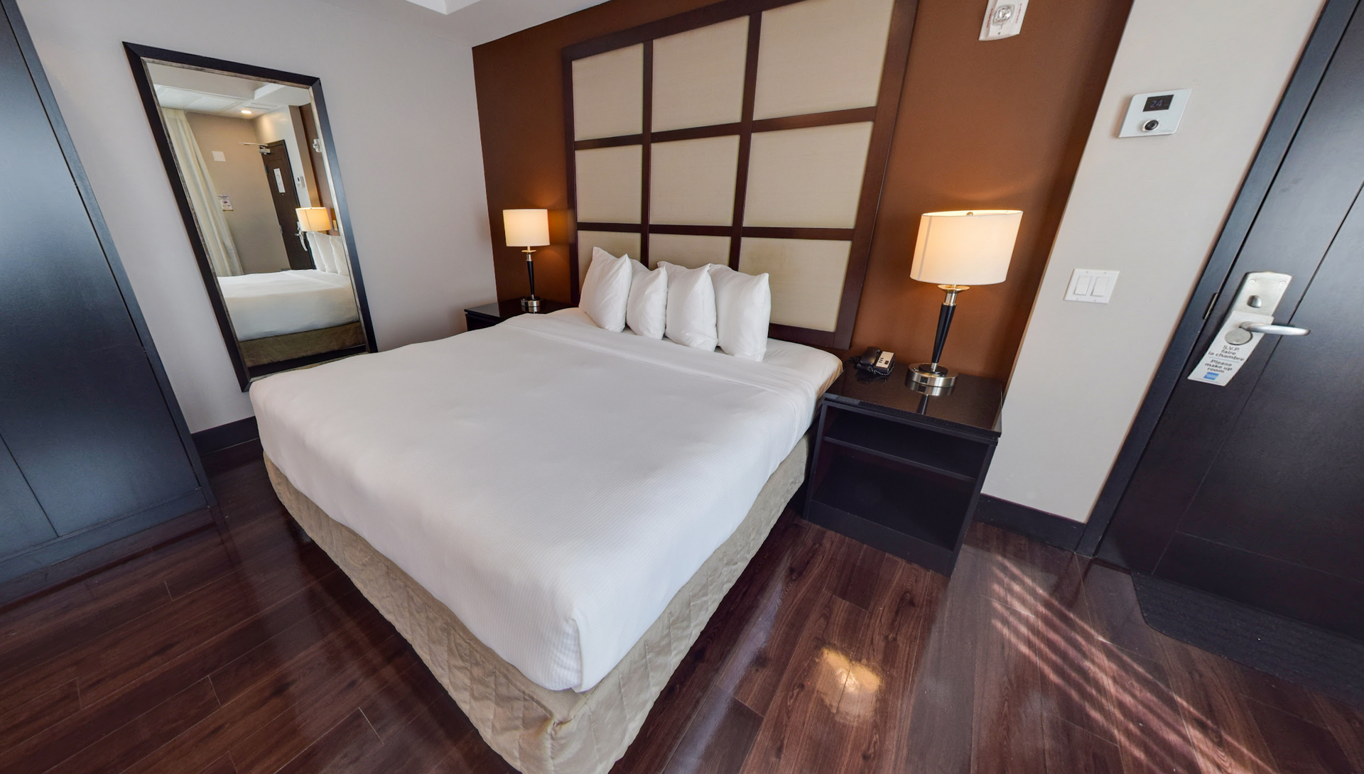 Chambre d'hôtel avec un grand lit, un miroir en pied, des tables de chevet avec lampes et un parquet.