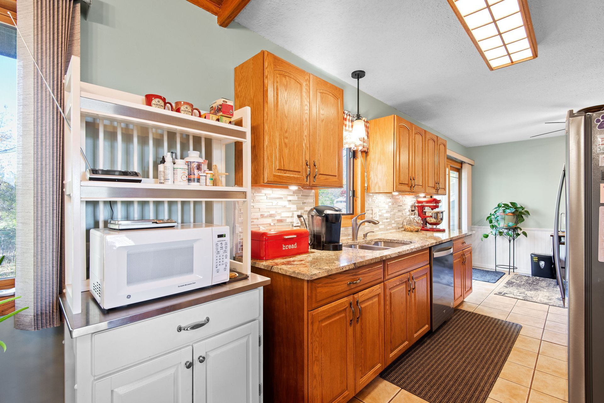 Bright galley kitchen with wooden cabinets, white appliances, and a skylight.