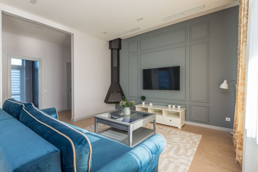 Modern living room with blue sofa, wall-mounted TV, fireplace, and gray paneled accent wall