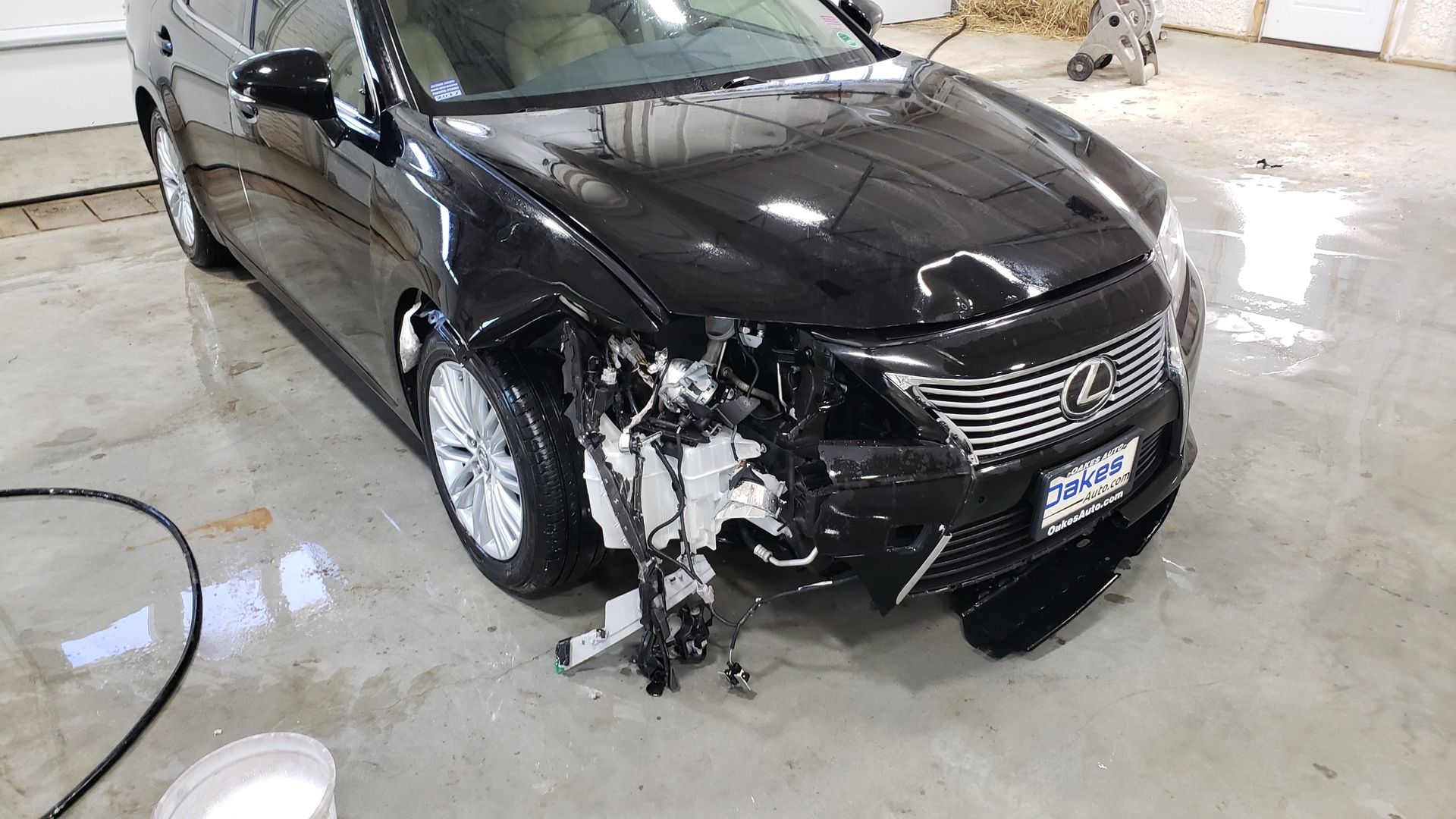 Black sedan with severe front-left collision damage in a garage or repair shop