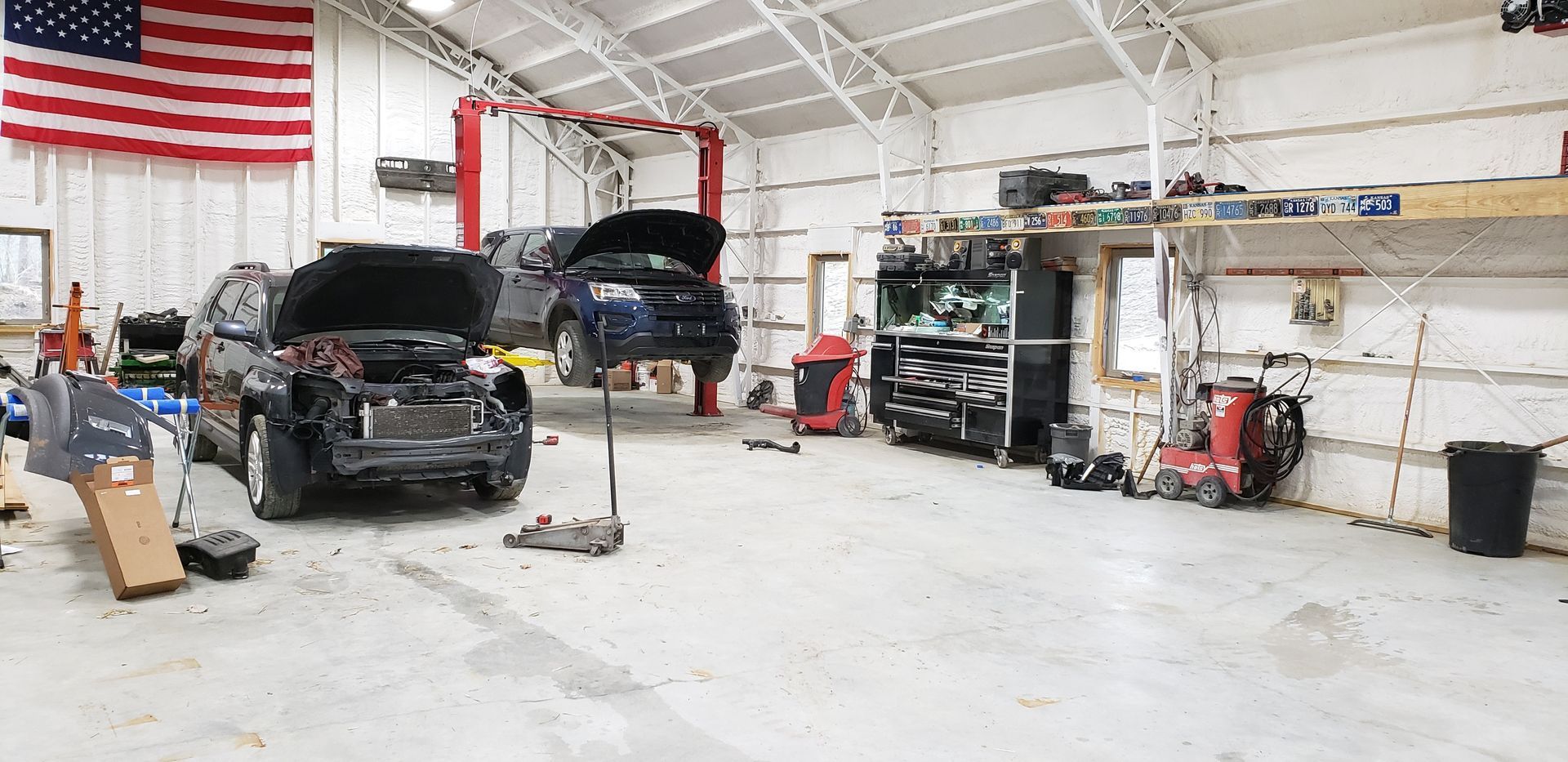 Auto repair shop with two cars under repair, tools, and a large American flag on the wall
