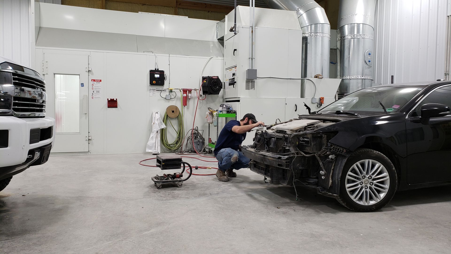 Auto body shop worker repairing a black car’s front end in a garage