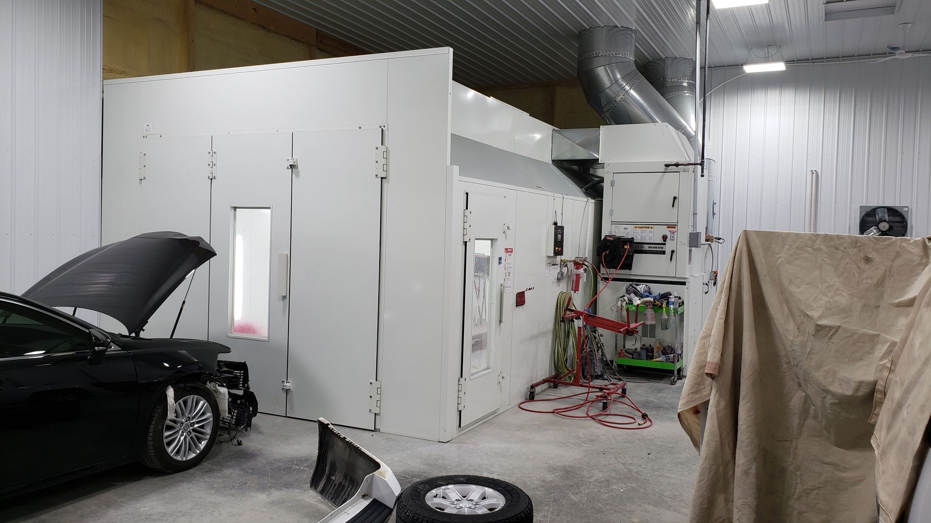 Auto body shop interior with a black car under repair and a white paint booth in the background