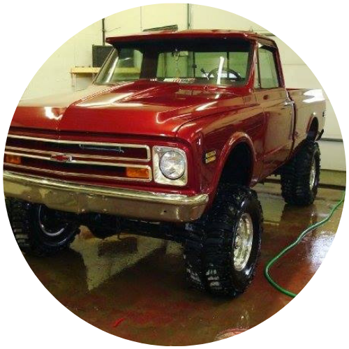 Red vintage pickup truck with lifted suspension, shown indoors on a wet floor.