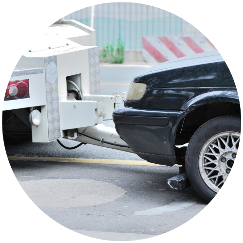 Black car bumper being pushed by a white tow truck in a street scene