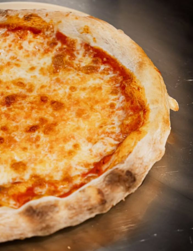 Primo piano di una pizza al formaggio su una superficie metallica, con una crosta croccante e formaggio fuso.