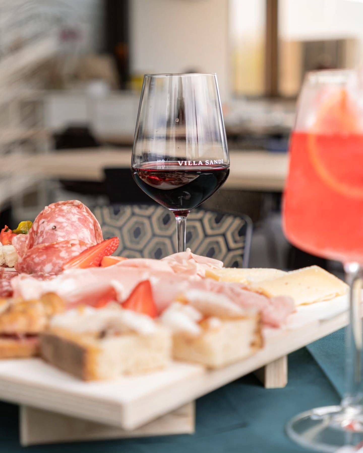 Un bicchiere di vino rosso, un tagliere di salumi con carne e pane e un cocktail in un ristorante.