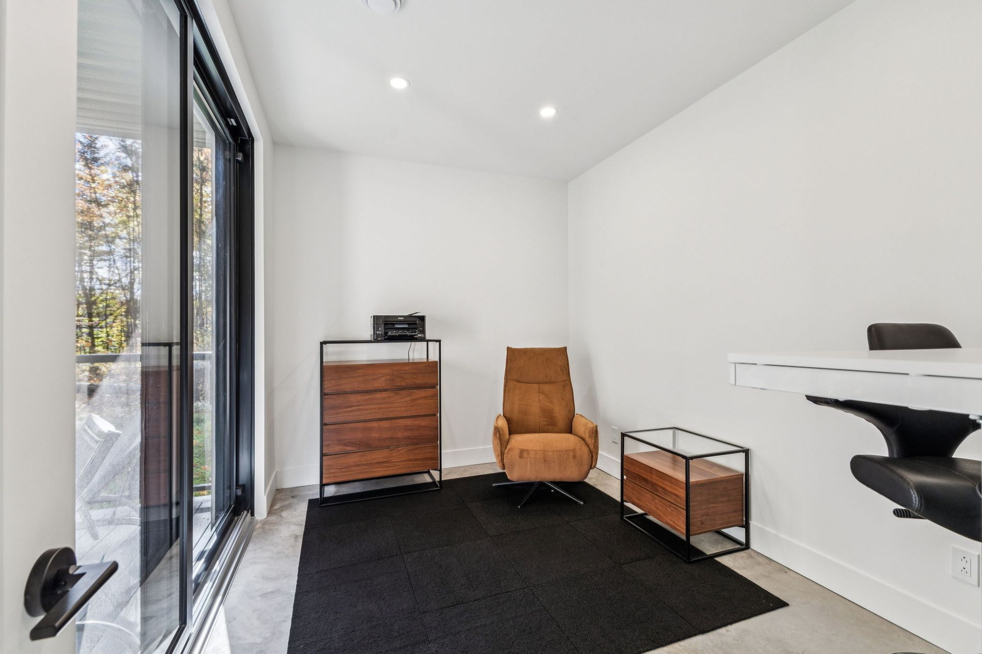 Une chambre moderne avec une chaise, un bureau et une grande fenêtre donnant sur un balcon.