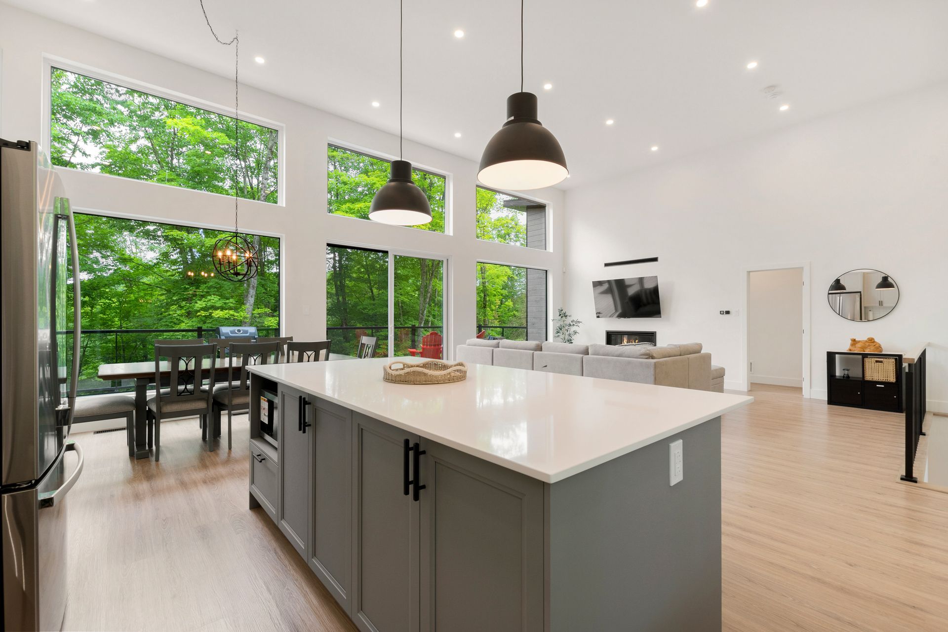 Cuisine spacieuse avec grand îlot central, baies vitrées donnant sur une végétation luxuriante. Design moderne, luminaires suspendus.