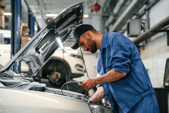 A man is working on a car in a garage with the hood up.