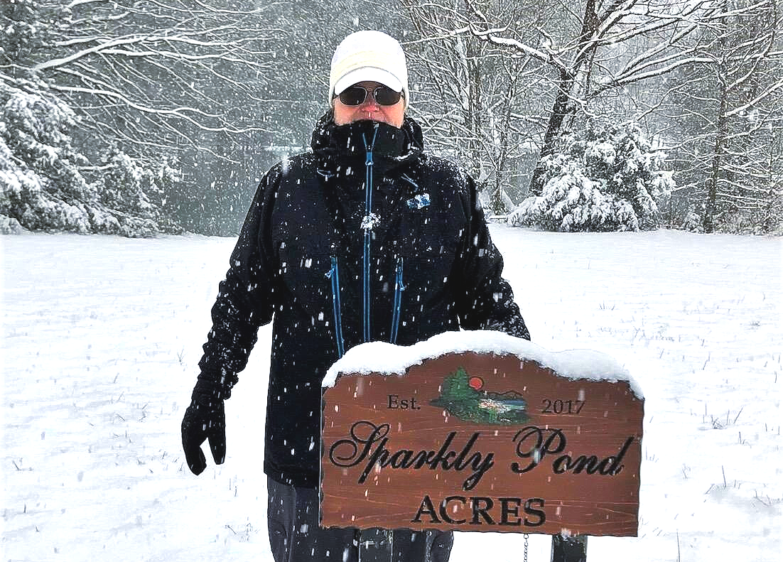 picture of lily ann fenwyn standing behind the sparkly pond acres sign while it is snowing