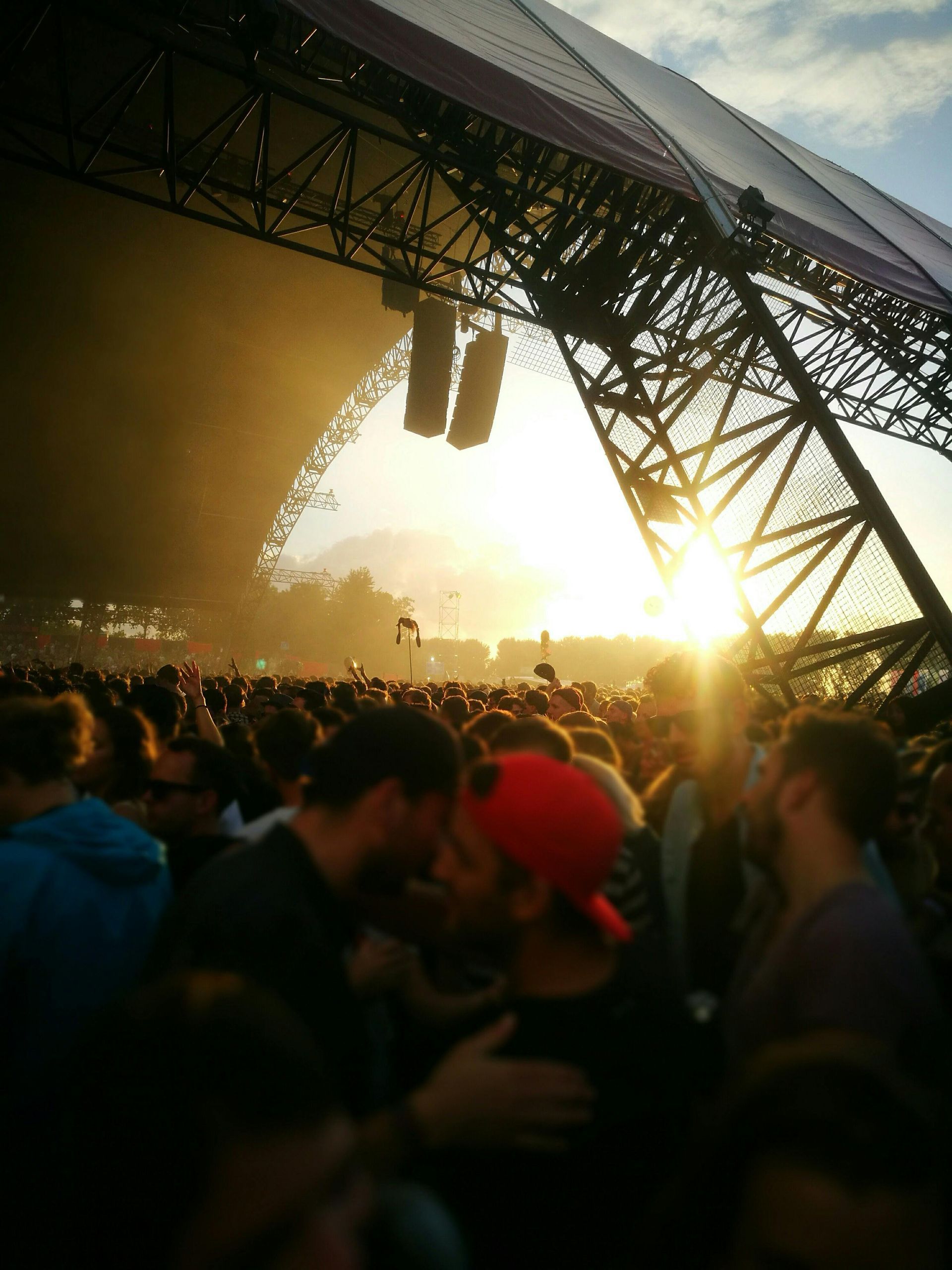Een groep mensen staat in tent met een ondergane zon voor een podium.
