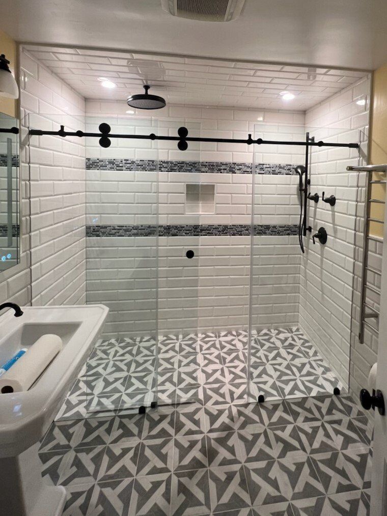 Modern bathroom with glass shower, black hardware, white and patterned gray tile.