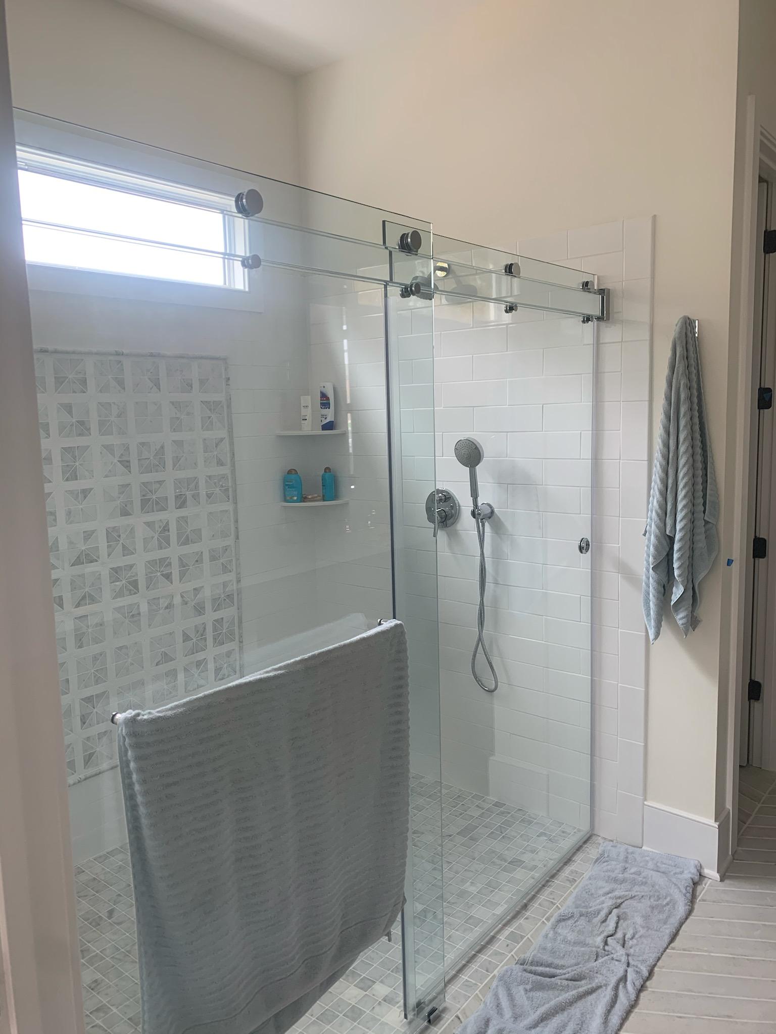 Glass shower with sliding door, white tile, stone floor, and towel rack.