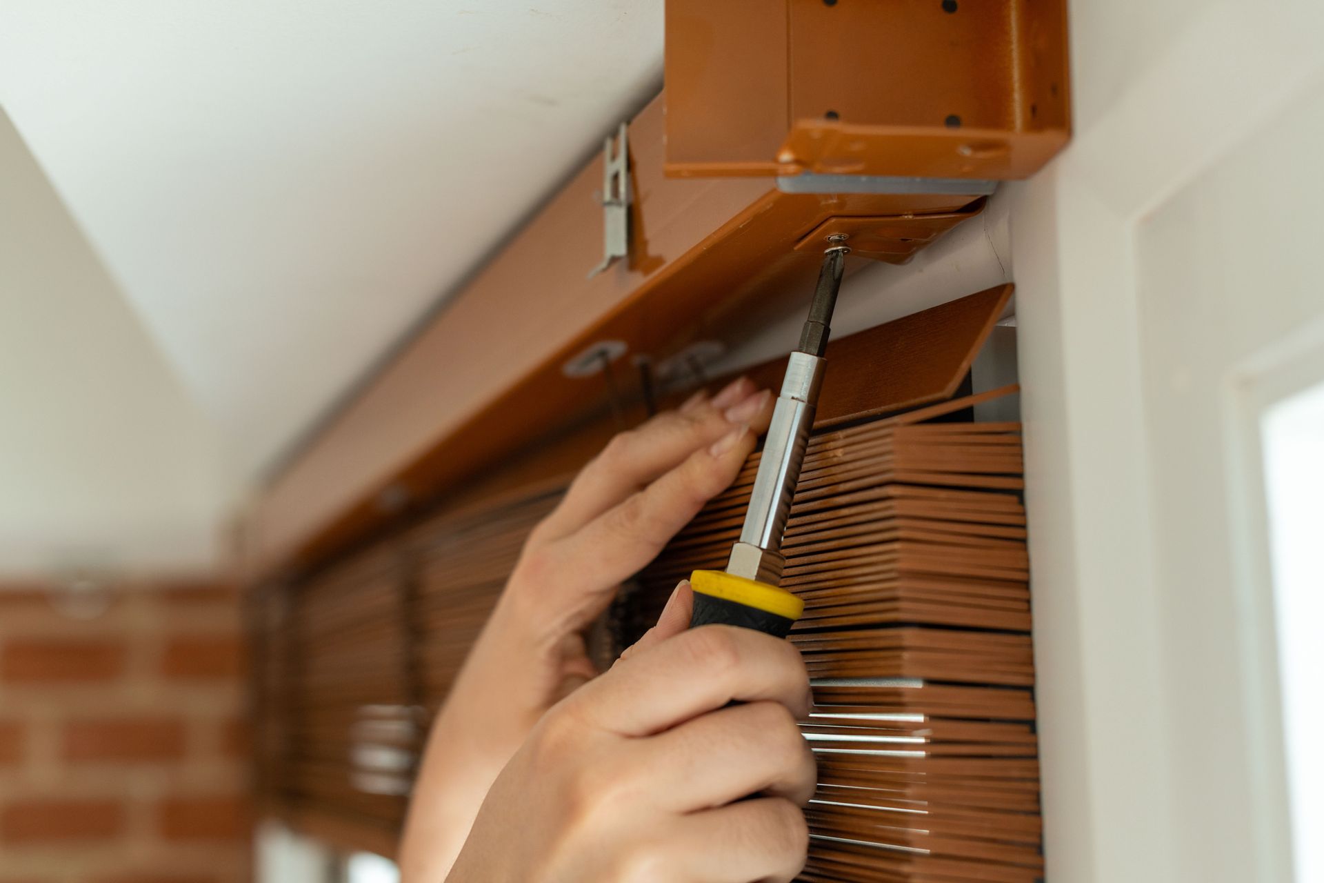 Hands using screwdriver to install or repair window blinds, adjusting mounting bracket.