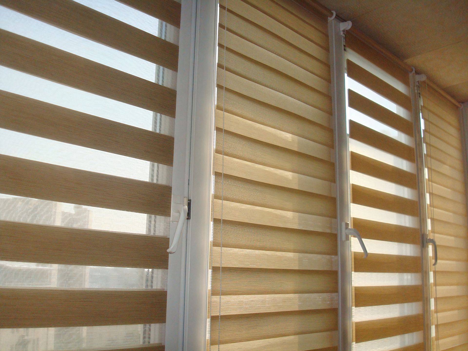 Tan dual-layer zebra roller blinds with alternating sheer and solid bands on white windows