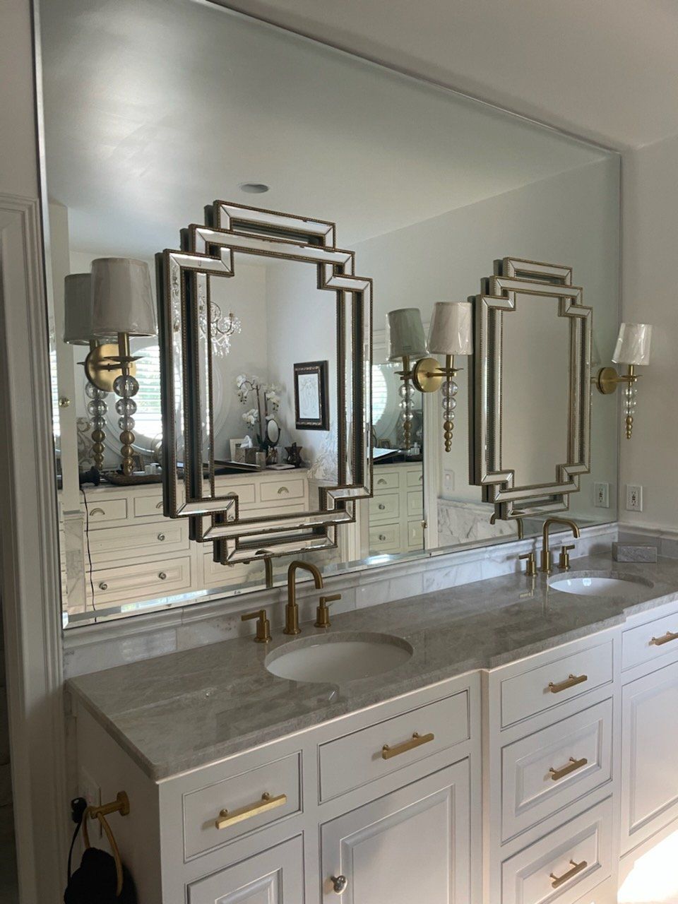Bathroom with white cabinets, marble countertop, gold fixtures, and large mirror with decorative frames.