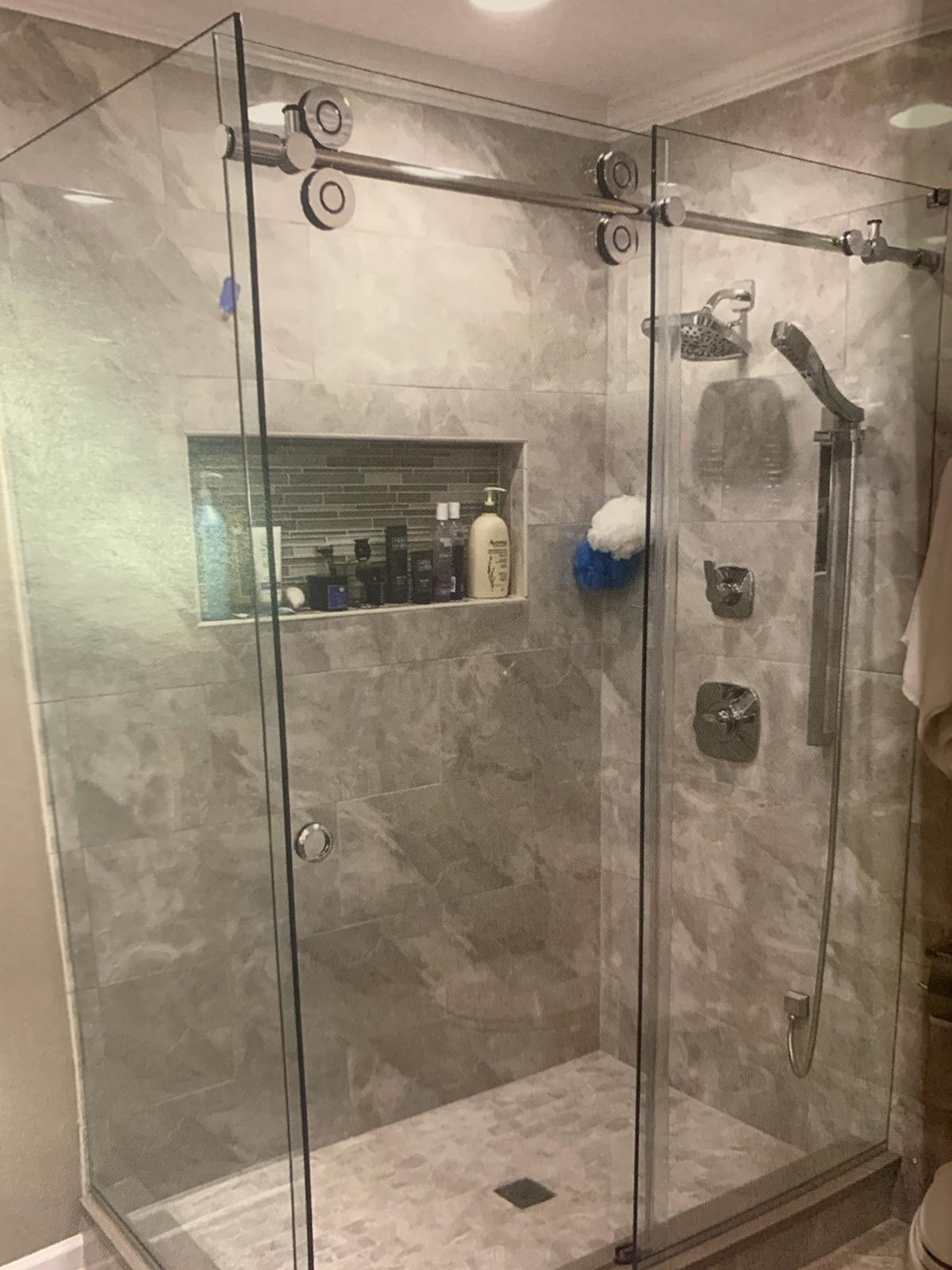 Glass shower enclosure with gray marble tile, sliding door, and recessed shelf.