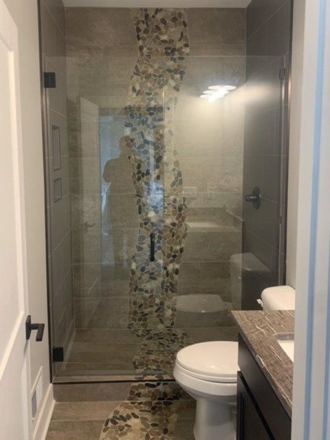 Bathroom with glass shower door, beige and stone accent wall, toilet, vanity, and white door.