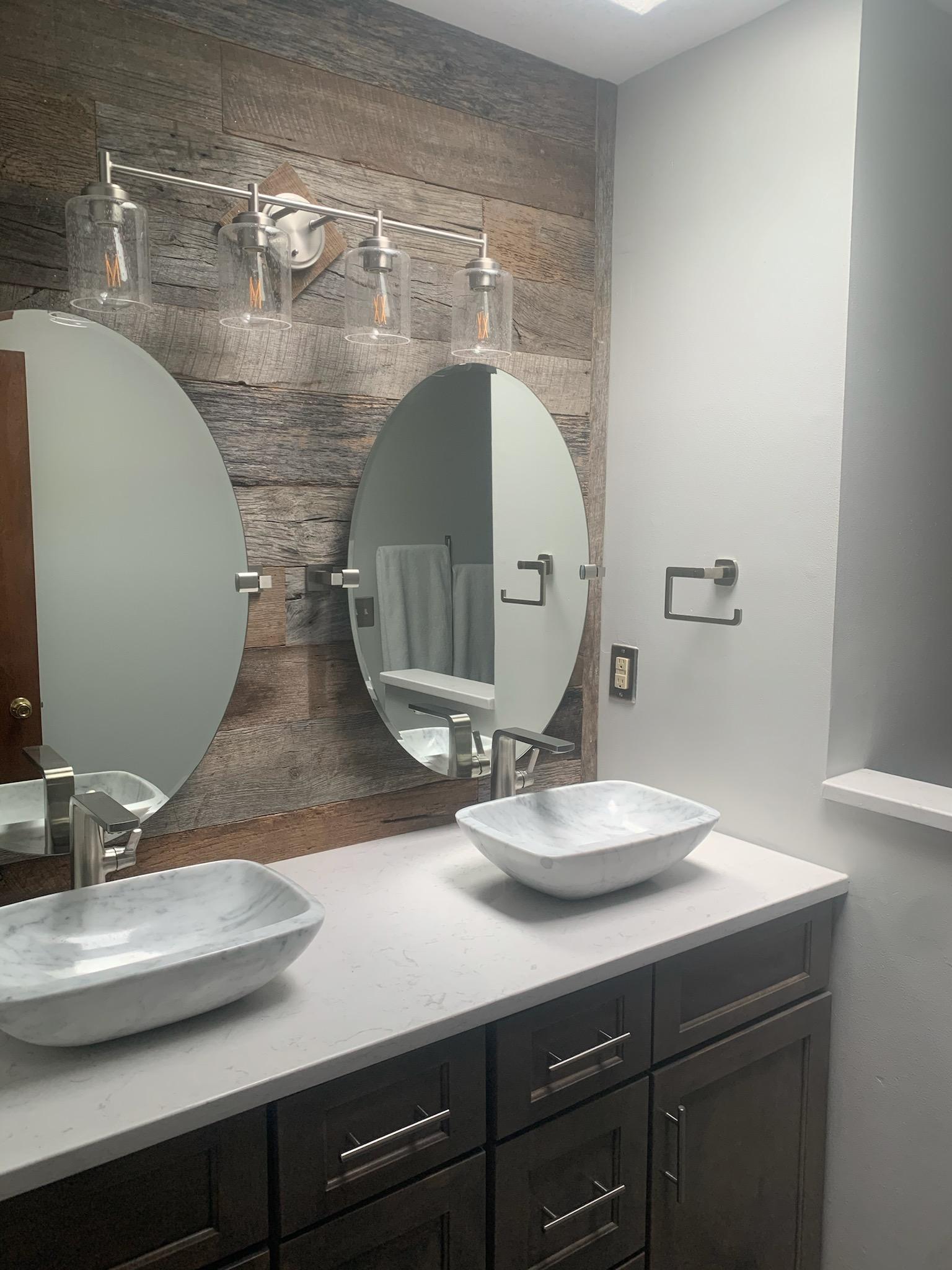 Double vanity bathroom with rustic wood accent wall, oval mirrors, and vessel sinks.