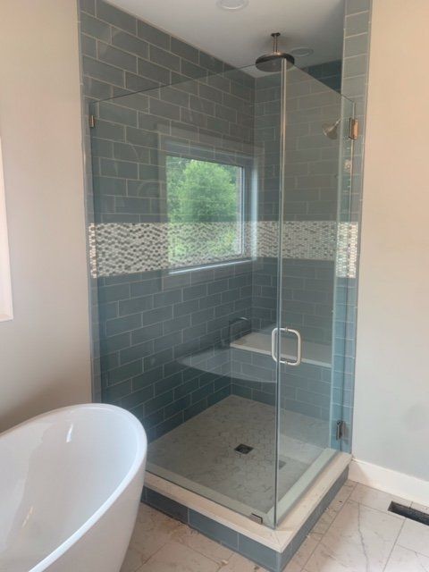 A modern bathroom with a glass shower, blue tile, and a white bathtub.