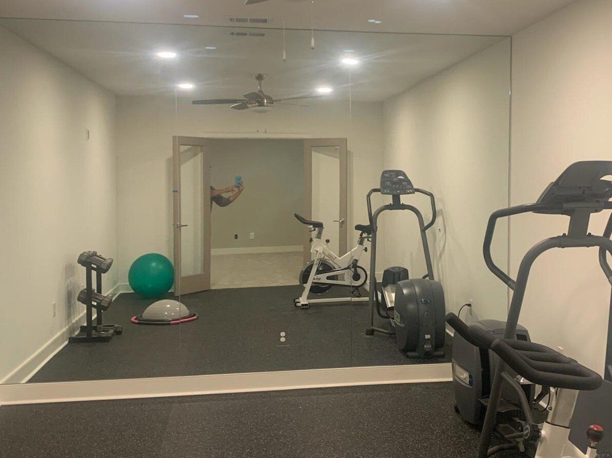 Home gym with exercise equipment, full wall mirror, and doorway to another room. Black floor.