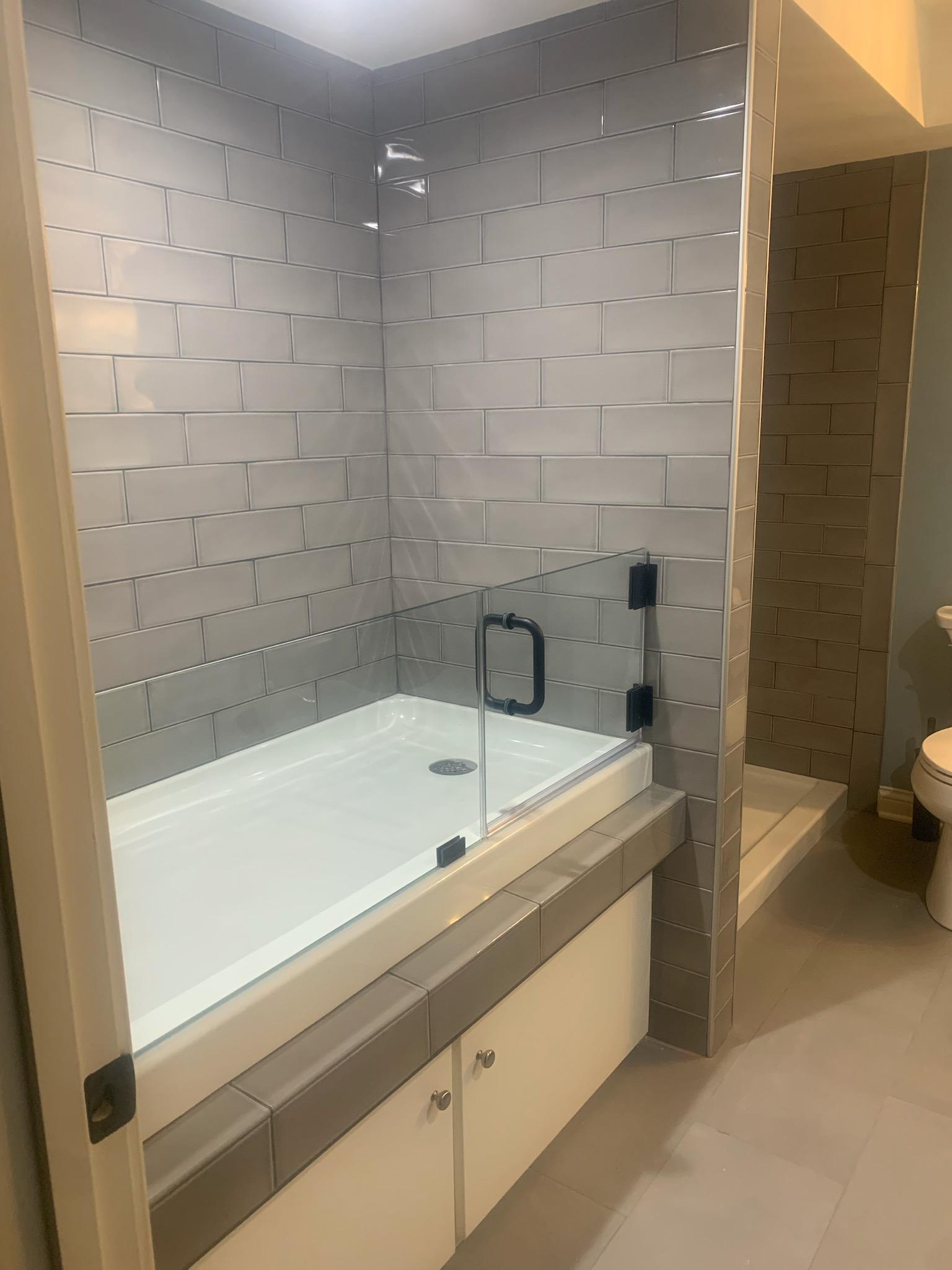 Shower stall with gray tile walls and a glass door.
