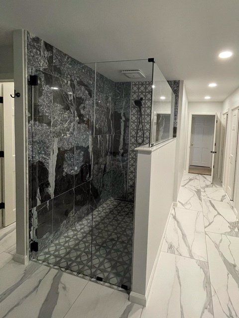 Modern bathroom with glass shower, dark gray accent tiles, marble floors, and a hallway.