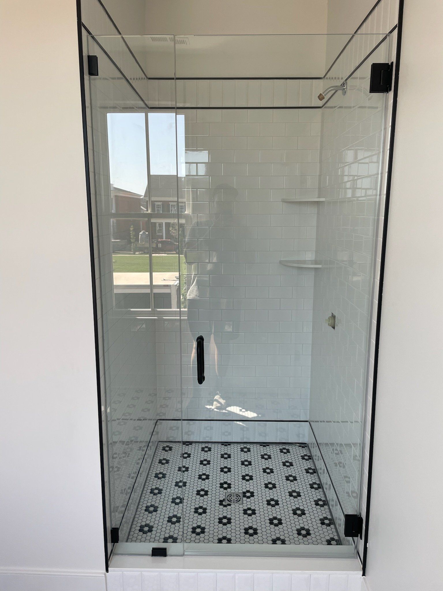 Glass shower with black trim and a patterned floor. The shower is built into a white-walled alcove.