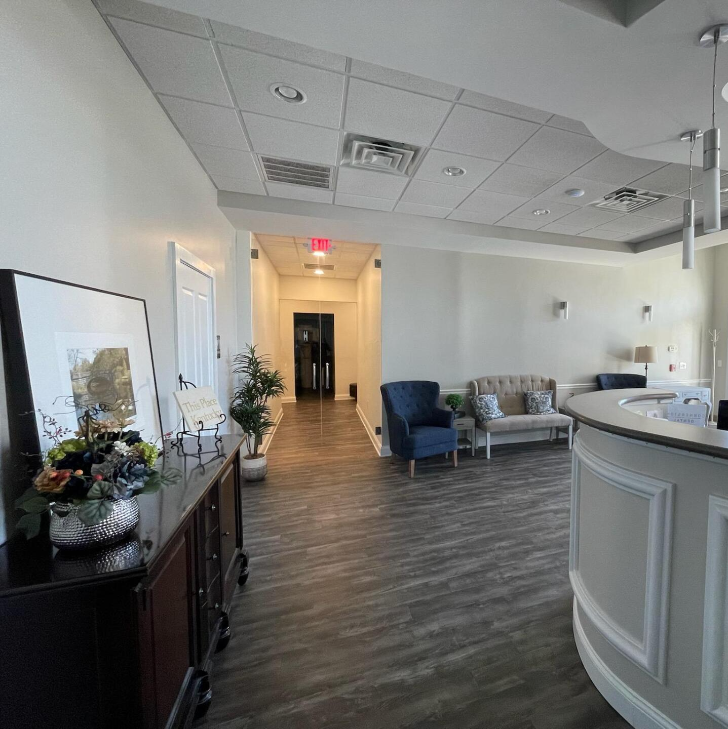 Spacious office lobby with dark wood floor, white walls, and a reception desk. Furnished with sofas and chairs.