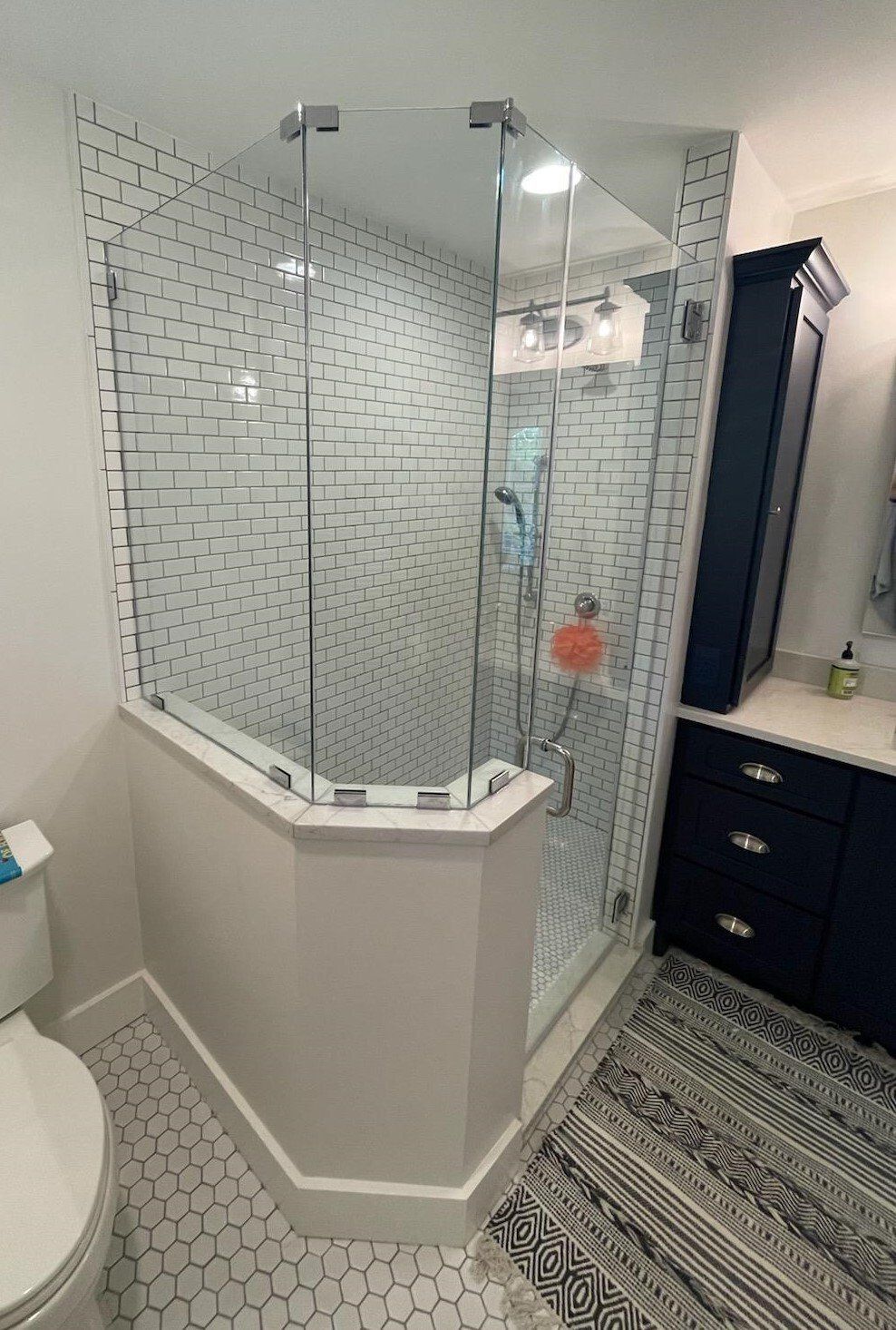 Bathroom with white walls, hexagon tiles, a glass shower, and a dark blue cabinet.