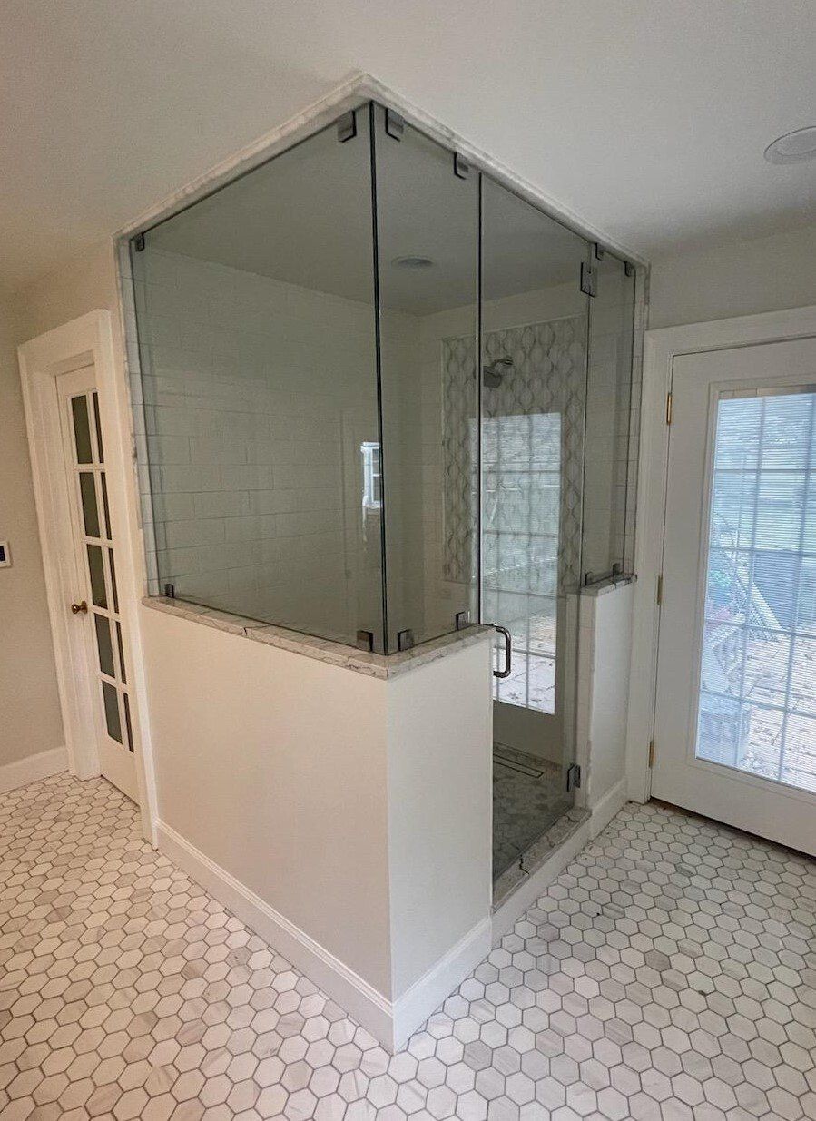 Corner shower with glass walls and a white tiled floor in a bathroom setting.